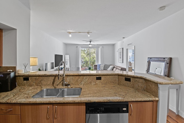 kitchen with kitchen peninsula, light stone counters, stainless steel dishwasher, ceiling fan, and sink