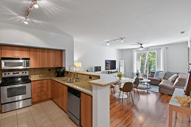 kitchen featuring kitchen peninsula, decorative backsplash, stainless steel appliances, ceiling fan, and sink