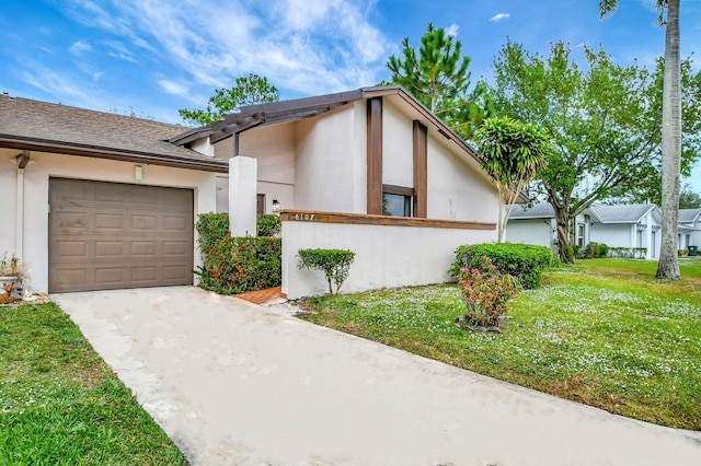 view of front of house with a garage, a front yard, concrete driveway, and stucco siding