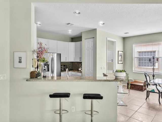 kitchen with stainless steel refrigerator, light tile patterned floors, kitchen peninsula, a breakfast bar area, and white cabinets