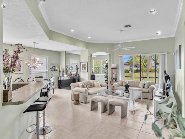 tiled living room with ceiling fan with notable chandelier and ornamental molding