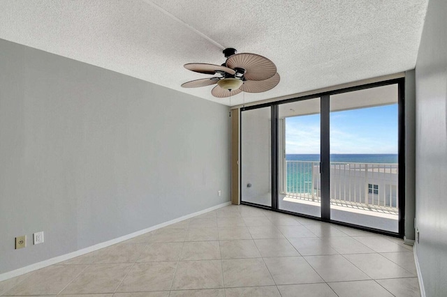 tiled spare room featuring expansive windows, ceiling fan, and a water view