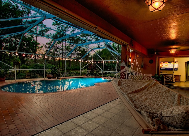 pool at dusk with a lanai and a patio area