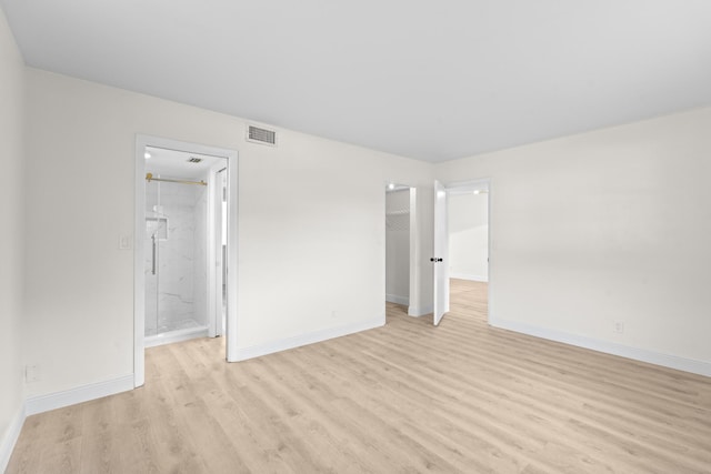 unfurnished bedroom featuring a walk in closet, light hardwood / wood-style flooring, and ensuite bath