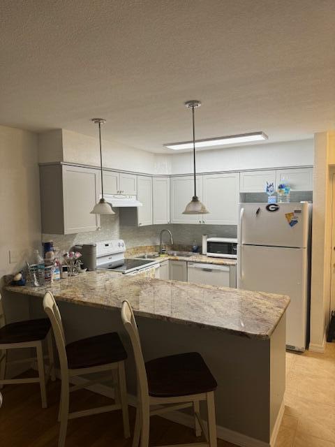 kitchen featuring kitchen peninsula, light stone countertops, hanging light fixtures, and white appliances