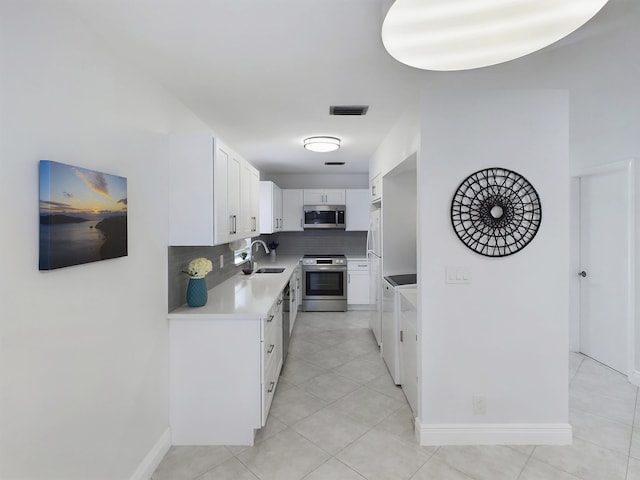 kitchen with appliances with stainless steel finishes, tasteful backsplash, sink, light tile patterned floors, and white cabinetry