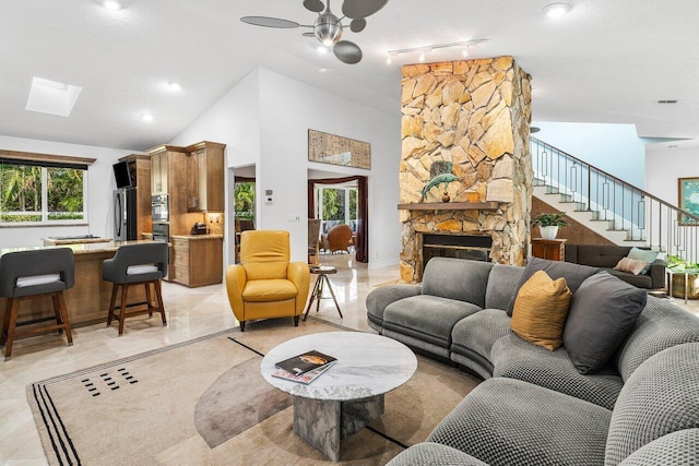 living room with a textured ceiling, ceiling fan, a fireplace, and high vaulted ceiling