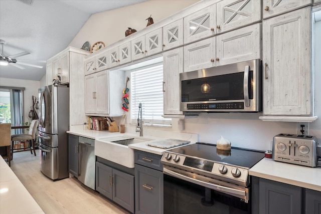 kitchen with appliances with stainless steel finishes, light wood-type flooring, sink, white cabinetry, and lofted ceiling