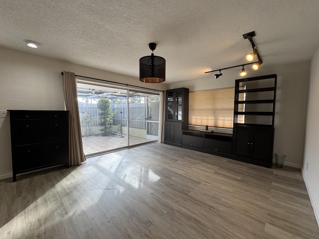 unfurnished living room with hardwood / wood-style flooring, a textured ceiling, and track lighting