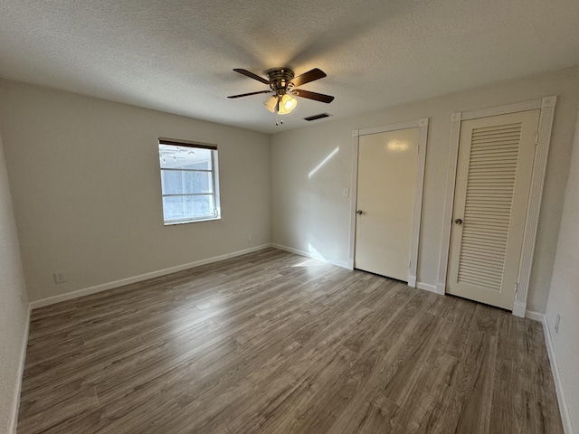 unfurnished bedroom with two closets, ceiling fan, hardwood / wood-style floors, and a textured ceiling