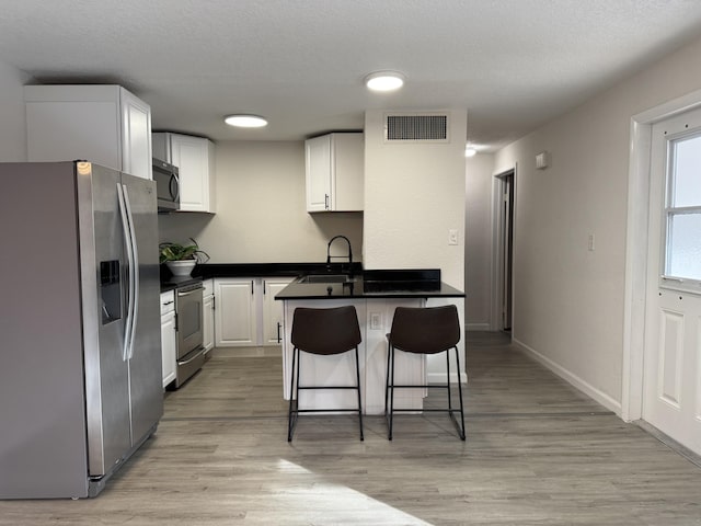 kitchen with white cabinetry, sink, light hardwood / wood-style floors, a kitchen bar, and appliances with stainless steel finishes