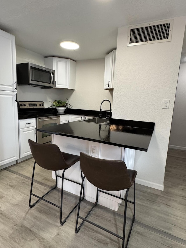 kitchen featuring kitchen peninsula, stainless steel appliances, white cabinetry, and sink