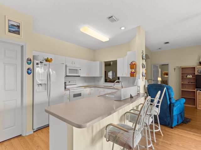 kitchen featuring kitchen peninsula, white appliances, sink, white cabinets, and light hardwood / wood-style floors