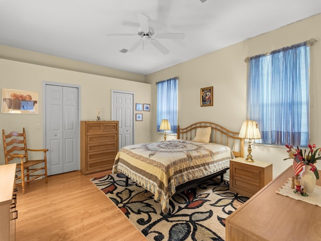 bedroom featuring ceiling fan, light hardwood / wood-style floors, and multiple closets