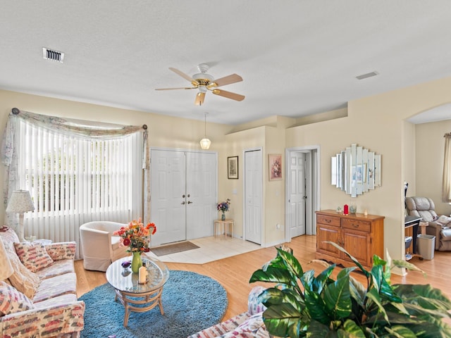 living room featuring ceiling fan, light wood-type flooring, and a textured ceiling