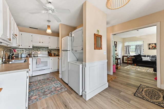 kitchen with white appliances, sink, light hardwood / wood-style flooring, stacked washer and clothes dryer, and white cabinets