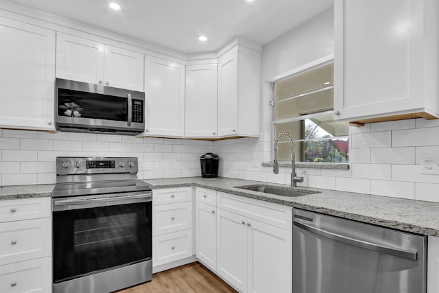 kitchen with white cabinets, sink, light stone countertops, and stainless steel appliances