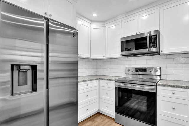 kitchen with light stone countertops, stainless steel appliances, white cabinetry, and light hardwood / wood-style floors