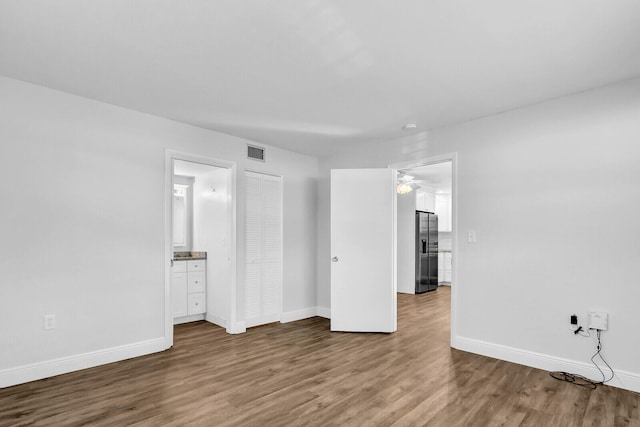 unfurnished bedroom featuring hardwood / wood-style floors, stainless steel fridge with ice dispenser, and connected bathroom