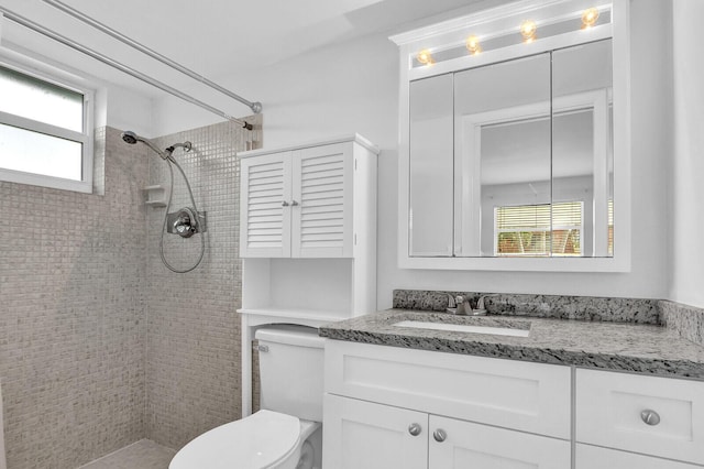 bathroom with a tile shower, vanity, toilet, and a wealth of natural light