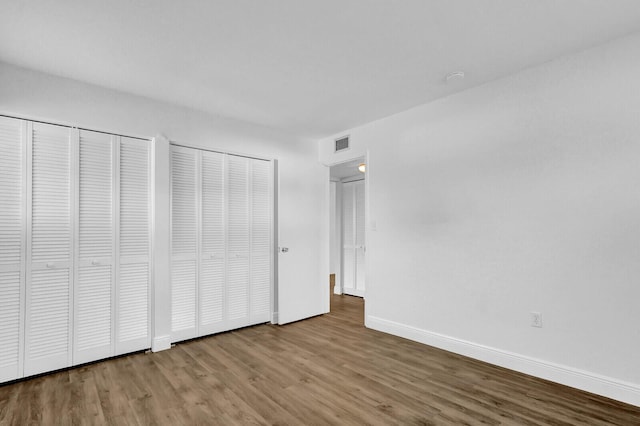 unfurnished bedroom with hardwood / wood-style flooring and multiple closets