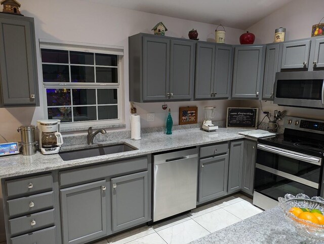 kitchen featuring sink, stainless steel appliances, light stone counters, lofted ceiling, and gray cabinets