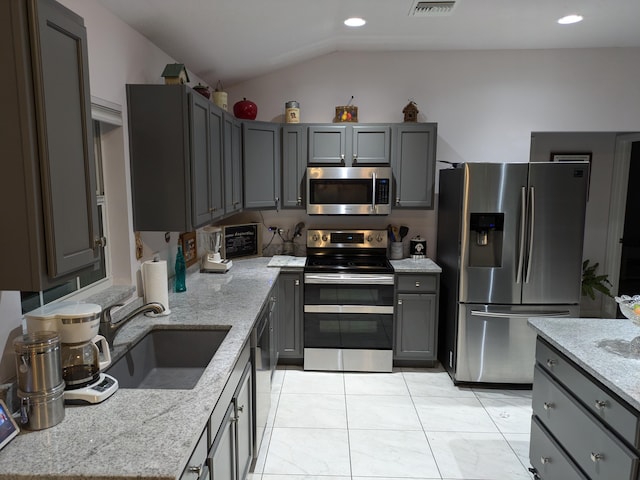 kitchen featuring sink, vaulted ceiling, appliances with stainless steel finishes, gray cabinets, and light stone countertops