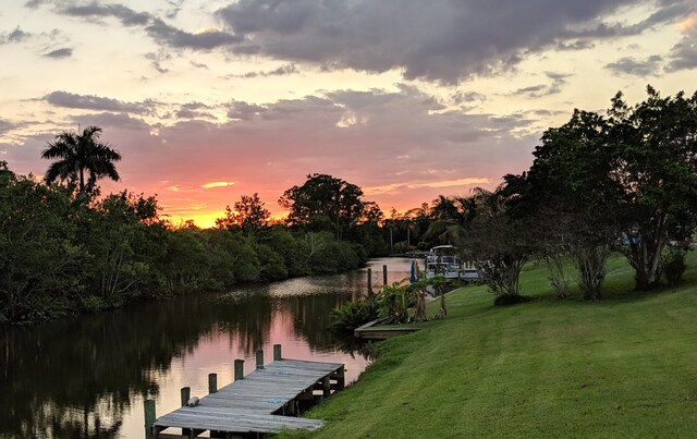 exterior space featuring a boat dock, a water view, and a lawn