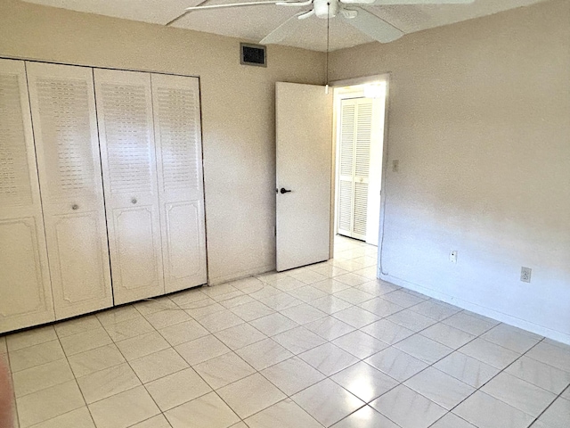 unfurnished bedroom with visible vents, a closet, light tile patterned floors, baseboards, and ceiling fan