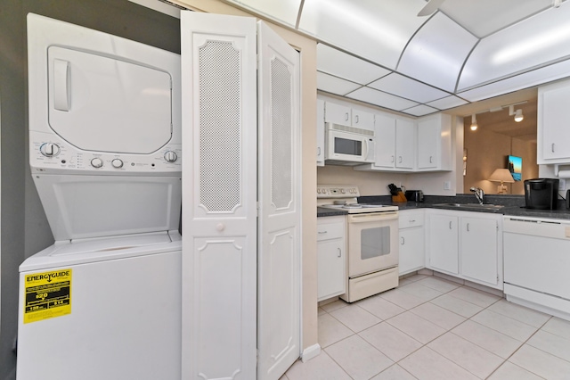 kitchen featuring stacked washer and dryer, white cabinets, white appliances, and sink