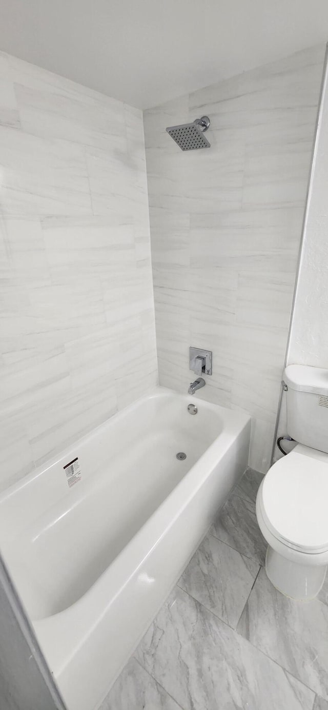 bathroom featuring tiled shower / bath combo, toilet, and tile walls