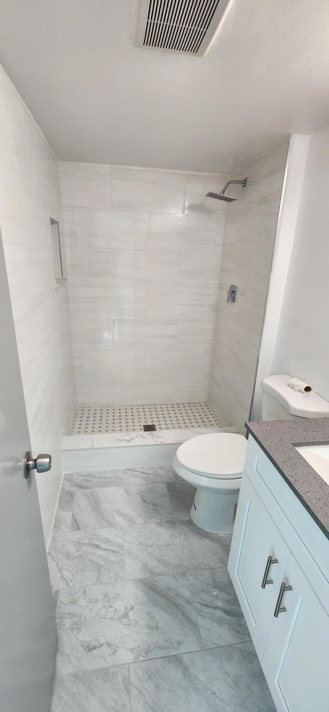 bathroom featuring toilet, vanity, and tiled shower