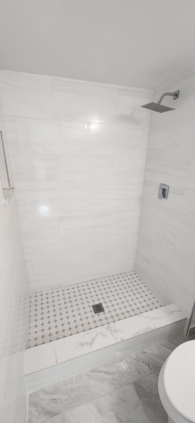 bathroom with a tile shower and toilet