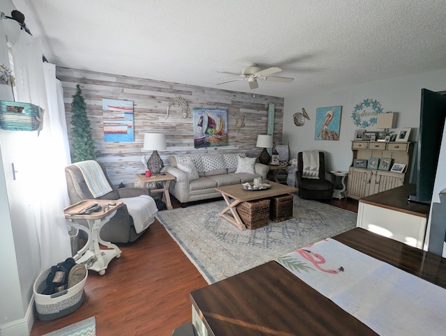 living room with dark hardwood / wood-style floors, wood walls, a textured ceiling, and ceiling fan