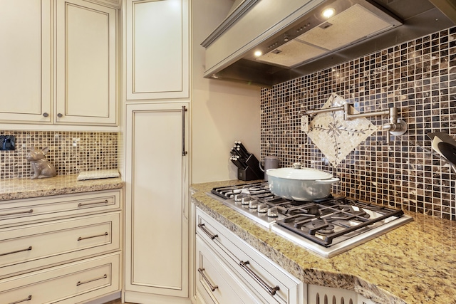 kitchen with custom range hood, stainless steel gas stovetop, light stone countertops, decorative backsplash, and cream cabinetry