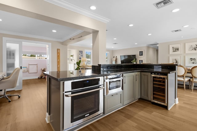 kitchen featuring dark stone countertops, oven, ornamental molding, beverage cooler, and light wood-type flooring