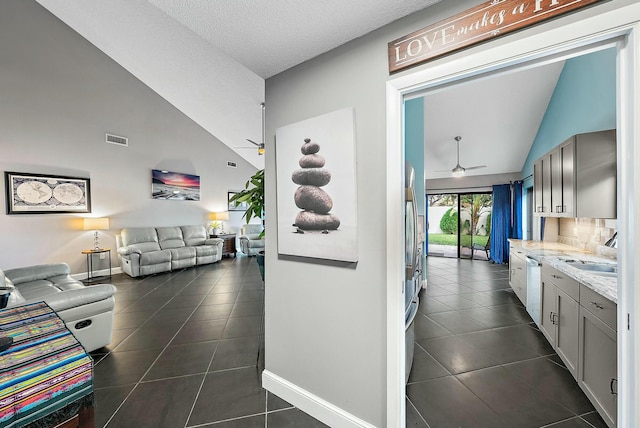 hallway with a textured ceiling, high vaulted ceiling, and dark tile patterned flooring