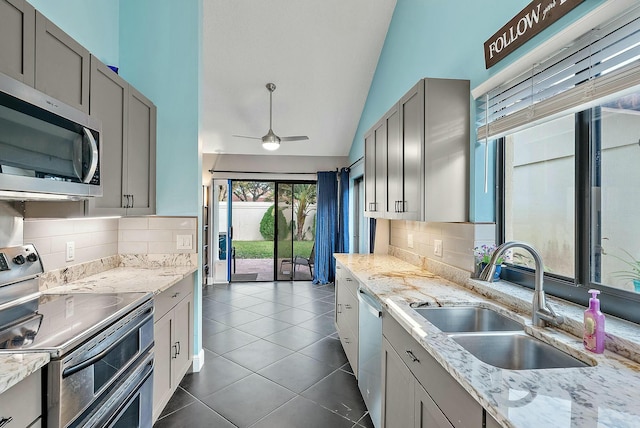 kitchen with gray cabinetry, sink, stainless steel appliances, backsplash, and lofted ceiling