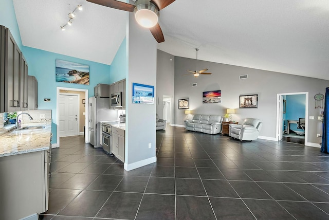 kitchen with sink, stainless steel appliances, light stone counters, high vaulted ceiling, and dark tile patterned flooring