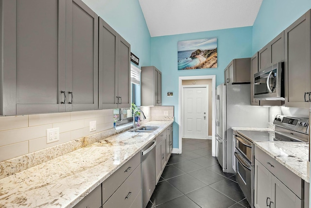 kitchen with light stone counters, stainless steel appliances, vaulted ceiling, dark tile patterned floors, and sink