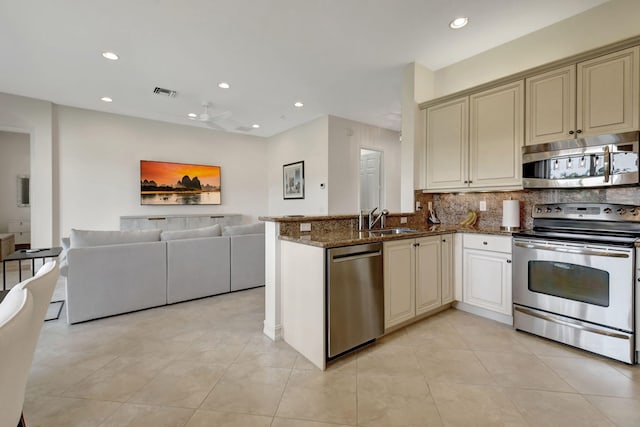 kitchen with dark stone counters, cream cabinets, decorative backsplash, kitchen peninsula, and stainless steel appliances