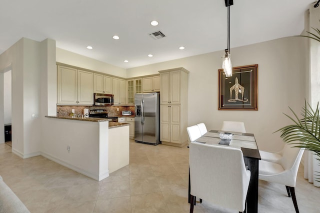 kitchen with hanging light fixtures, stainless steel appliances, tasteful backsplash, kitchen peninsula, and cream cabinetry