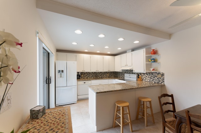 kitchen with kitchen peninsula, dark stone countertops, white cabinets, and white appliances