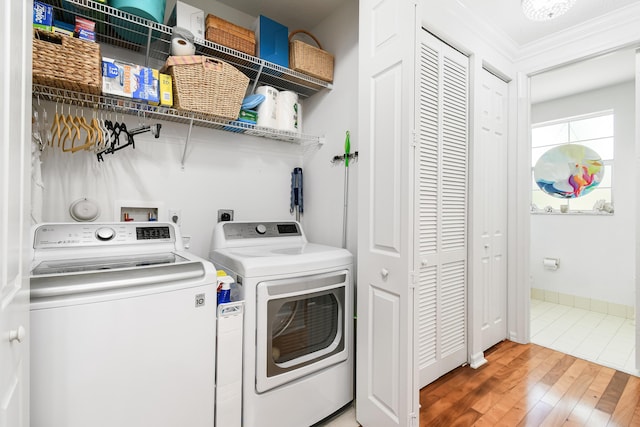 clothes washing area with washing machine and clothes dryer, crown molding, and hardwood / wood-style floors