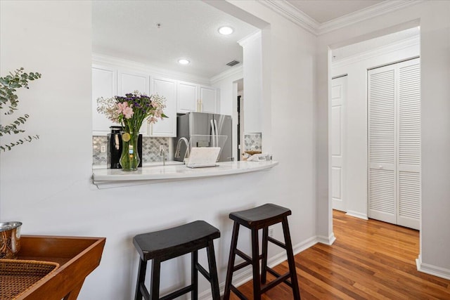 kitchen featuring a kitchen breakfast bar, ornamental molding, hardwood / wood-style flooring, white cabinetry, and stainless steel refrigerator