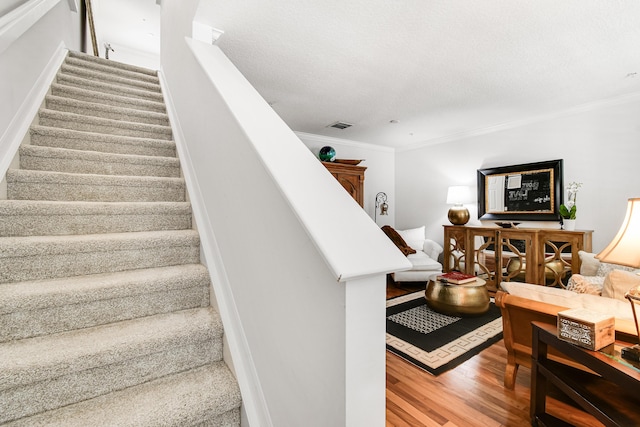 staircase with a textured ceiling, wood-type flooring, and crown molding