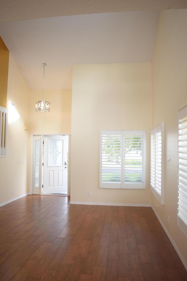 foyer entrance with dark wood-type flooring, high vaulted ceiling, and an inviting chandelier