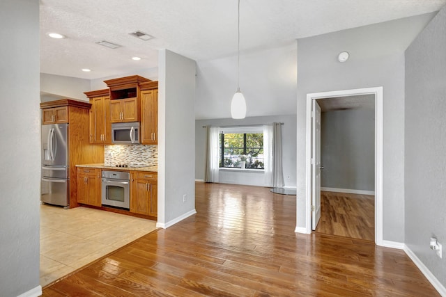 kitchen featuring light hardwood / wood-style flooring, decorative backsplash, a textured ceiling, decorative light fixtures, and stainless steel appliances