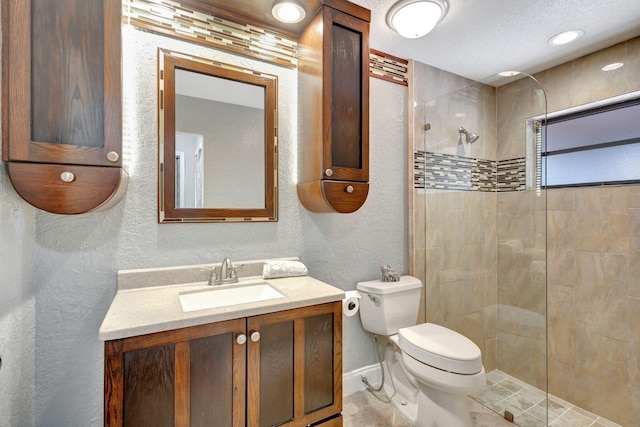 bathroom with a textured ceiling, vanity, toilet, and tiled shower