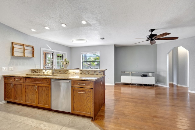 kitchen with ceiling fan, sink, light hardwood / wood-style flooring, stainless steel dishwasher, and a textured ceiling